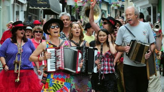 A group of men and women playing different instruments including a harmonium, flute and horn outdoors.